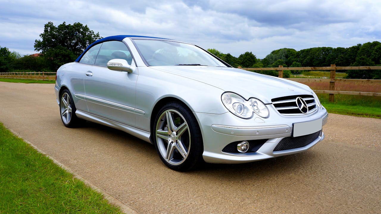 A silver convertible sports car parked on a countryside road under an overcast sky.