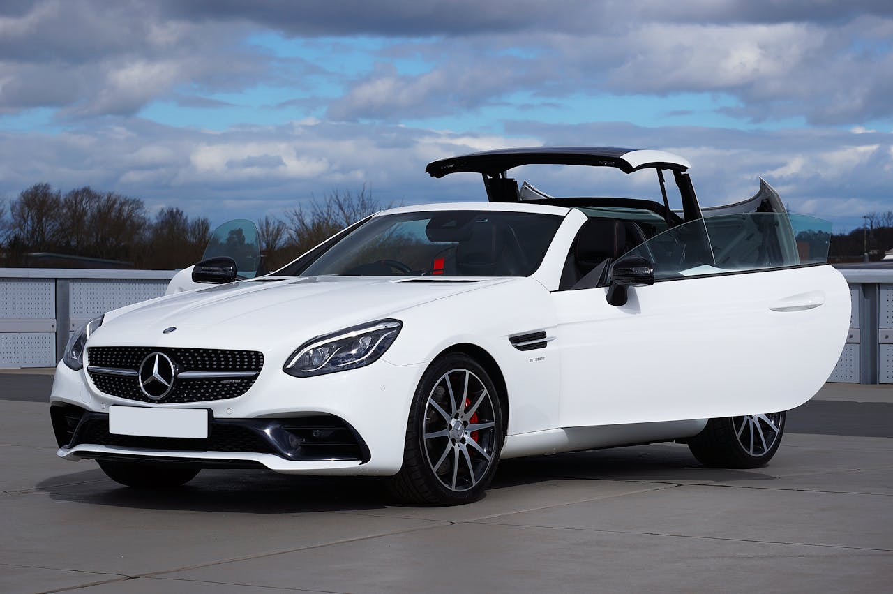 Stylish white convertible car with open roof displayed outdoors on a cloudy day.