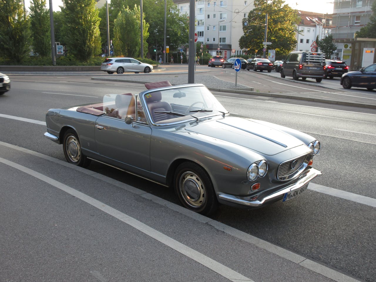 Vintage convertible car parked on an urban road during daytime traffic.