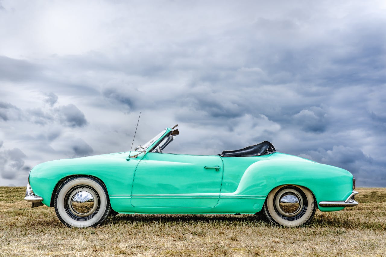 Mint green classic convertible parked in open field under a cloudy sky.